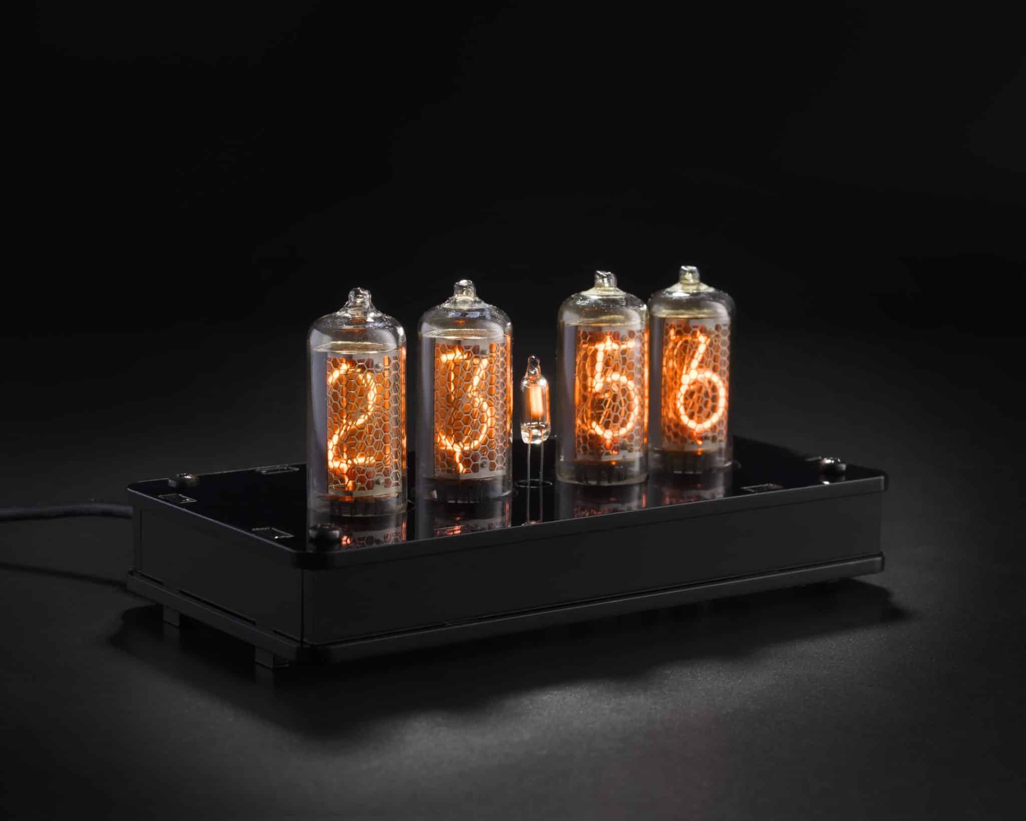 Four illuminated IN-8 Nixie tubes in a black acrylic clock case, viewed at an angle.
