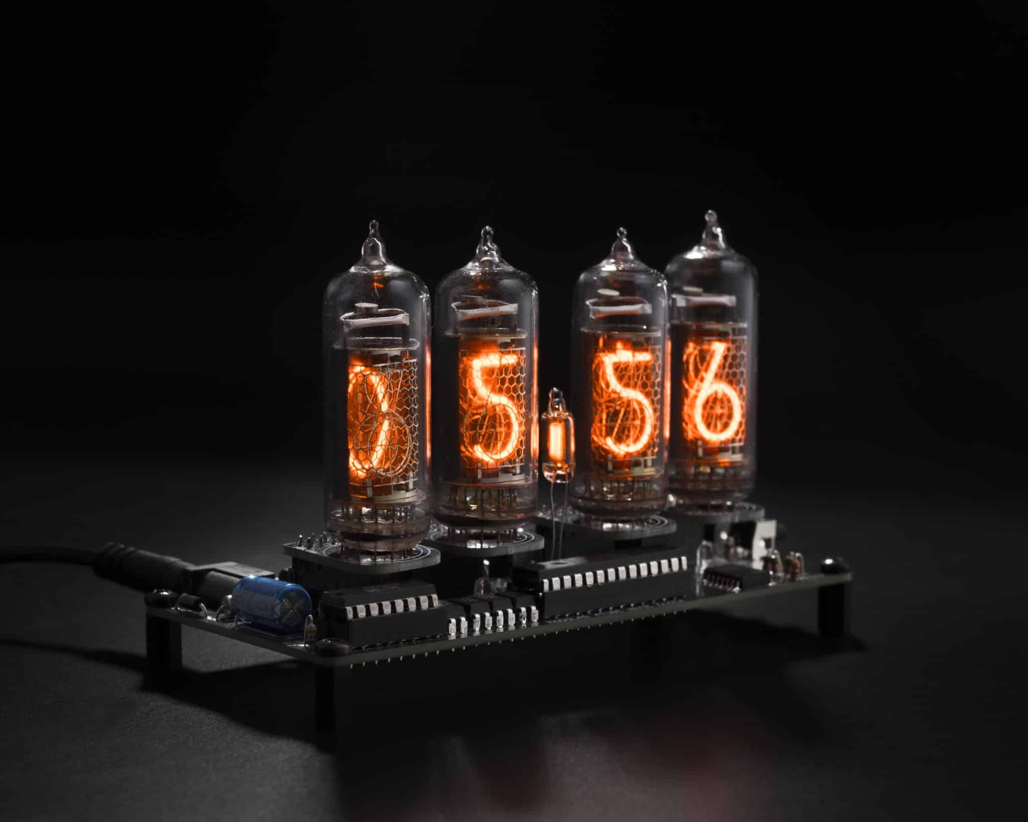 Four glowing Nixie tubes mounted on removable modules above the exposed clock controller board.