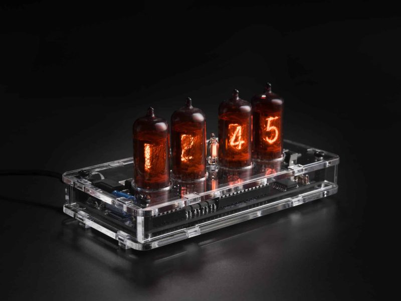 Four red-coated Z573M Nixie tubes in a transparent acrylic clock case, viewed at an angle.